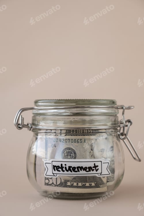 Preview: Saving Money In Glass Jar filled with Dollars banknotes. RETIREMENT transcription in front of jar