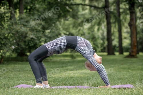 Preview: An elderly woman in sportswear does yoga on a mat outdoors.