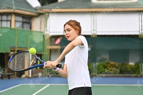 Preview: Shot of young female athlete hitting tennis ball flying towards her.