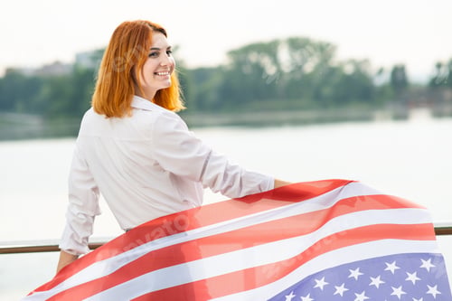 Preview: Happy red haired girl with USA national flag on her shoulders.