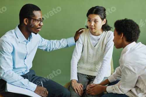 Preview: Young African American psychologist supporting Asian schoolgirl at session