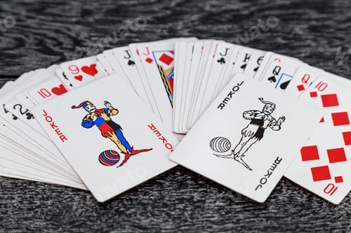 Preview: two jokers and a scattered deck of playing cards is on a gray wooden table