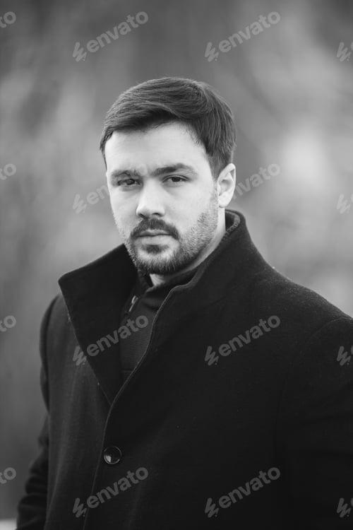 Preview: Vertical shot of a handsome Caucasian male with a black coat posing outdoors