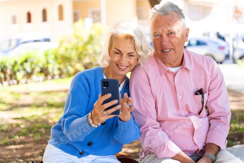 Preview: Smiling senior couple using smartphone outdoors in urban park