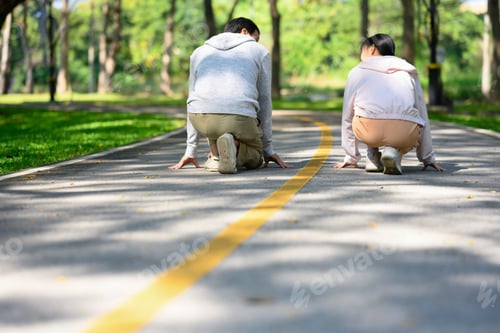 Preview: Senior man and young adult daughter crouching down in starting position on paved pathway in a park