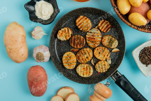 Preview: top view of fried potato slices in frying pan with uncooked ones in basket, mayonnaise, garlic, salt