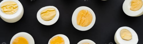 Preview: Top view of cut boiled eggs with yolks on black background, banner