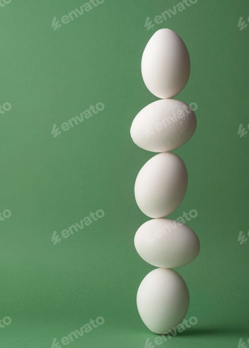 Preview: Five white eggs balancing in a vertical line on green background