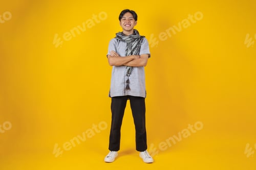 Preview: Full Body Shot of Young Asian Muslim Man Crossed Arms Over Yellow Background