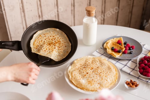 Preview: Hand of young female with frying pan taking hot appetizing pancake while cooking