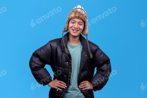 Preview: Confident young man wearing winter clothing with hands on hips isolated on blue background