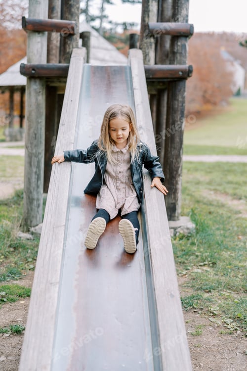 Preview: Little girl slides down a slide on a playground holding the handrails