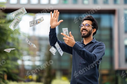 Preview: Overjoyed rich young indian businessman throwing money dollar banknotes