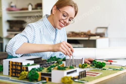 Preview: Photo of joyful young woman architect designing draft with house model