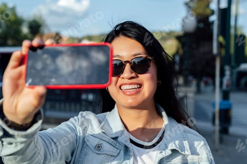 Preview: Asian woman with sunglasses taking a selfie with the phone in the city