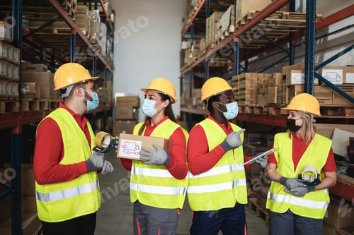 Preview: Happy workers talking inside warehouse while wearing safety masks