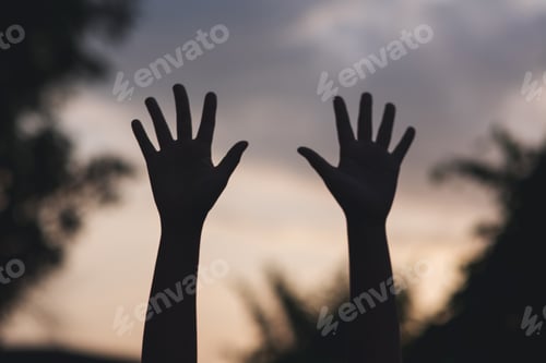 Preview: Silhouette of two hands raise with blurred sunset sky background
