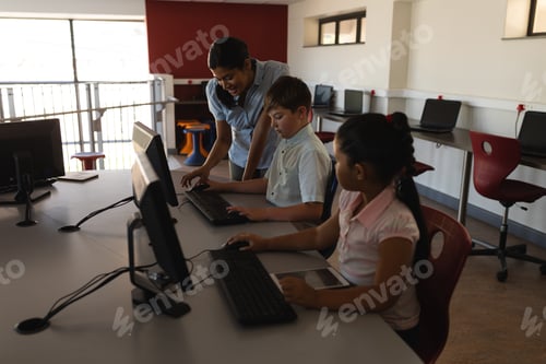 Preview: Side view of female teacher teaching computer to schoolkid at desk in school