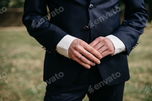 Preview: Man in suit with clasped hands outdoors.