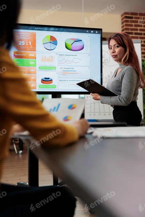Preview: Businesswoman explaining management statistics to asian manager