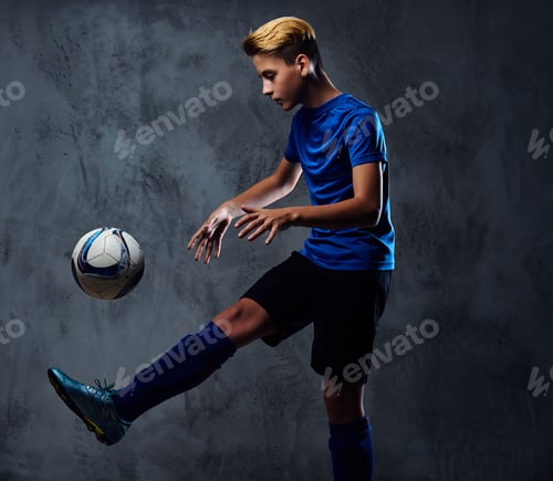 Preview: Teenager soccer player dressed in a blue uniform plays with a ball.