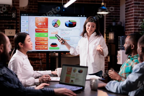 Preview: Smiling caucasian woman in startup office looking at team sitting at desk explaining marketing