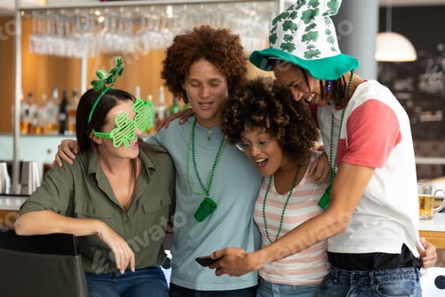 Preview: Diverse group of happy friends celebrating st patrick's day looking at smartphone at a bar