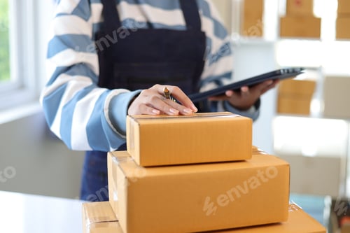 Preview: Young Asian woman starting an online sales business at home holding a tablet analyzing sales.