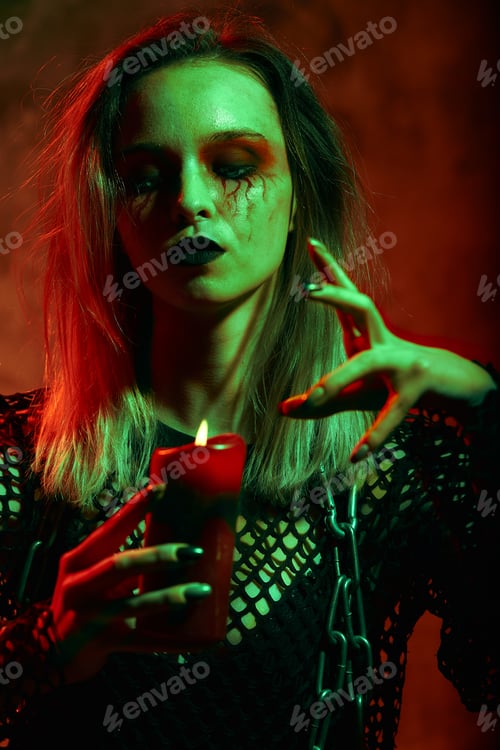 Preview: close up portrait of beautiful sexy witch with halloween makeup. red and black face painting.candle