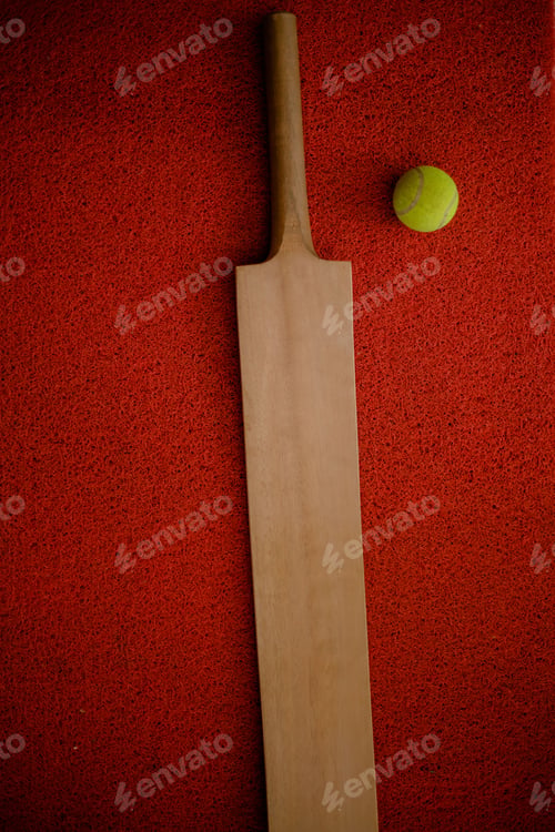 Preview: Vertical closeup top view of a cricket bat and a ball on a red surface