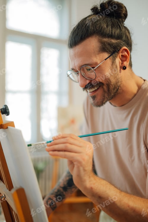 Preview: Smiling artistic painter painting on easel at creative art studio.