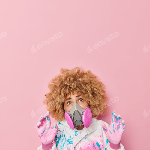 Preview: Curly haired female worker wears hazmat suit and gas mask keeps hands raised trying to protect herse