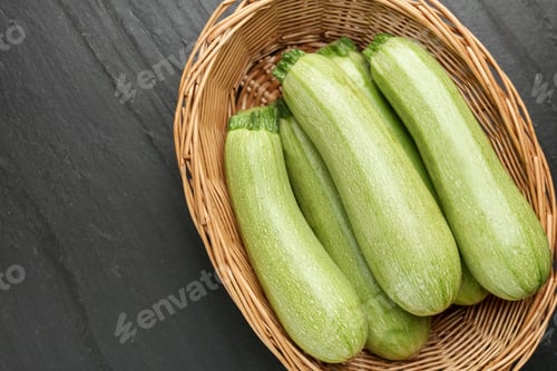 Preview: Fresh ripe zucchinis in wicker basket on black textured table, top view. Space for text