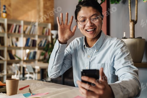 Preview: Image of smiling asian man using cellphone and waving hand
