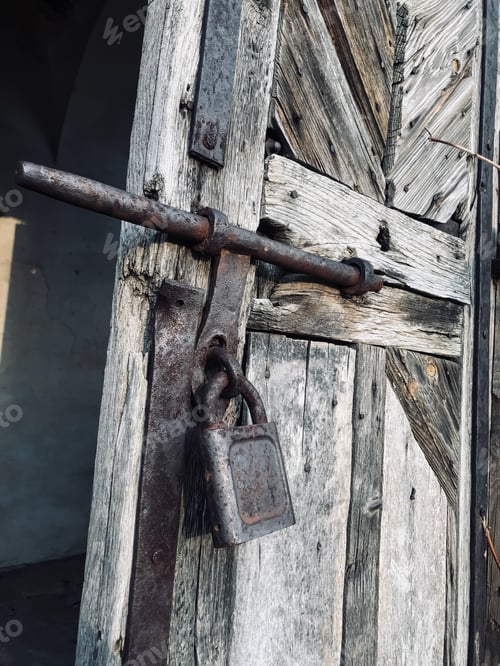 Preview: An metal large rusty padlock is hanging on the wooden doors