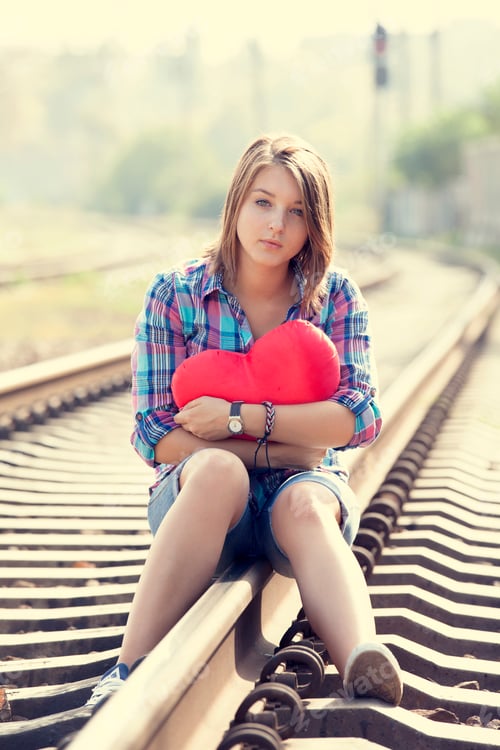 Preview: Sad teen girl with heart sitting at railway.
