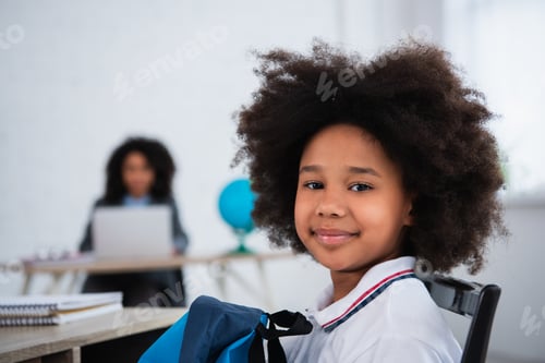 Preview: African american schoolkid with backpack looking at camera in classroom