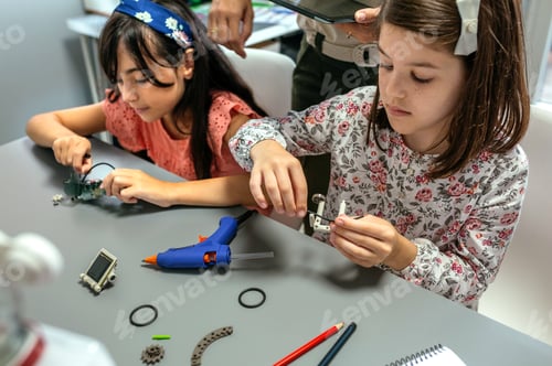 Preview: Students assembling machine pieces with teacher helping their in a robotics class.