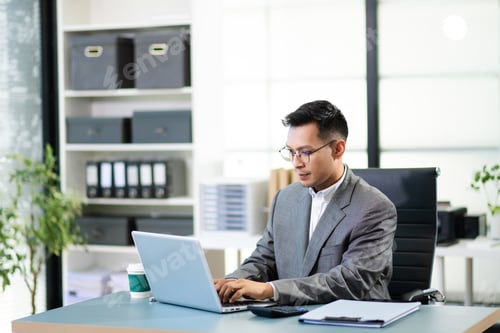 Preview: Asian man using laptop and tablet while sitting at her working place. Concentrated at work.