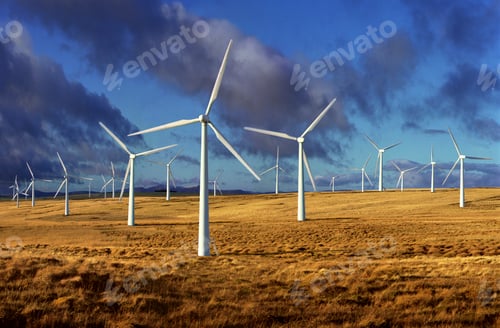 Preview: Wind turbines standing tall over a sprawling golden field under a bright blue sky.