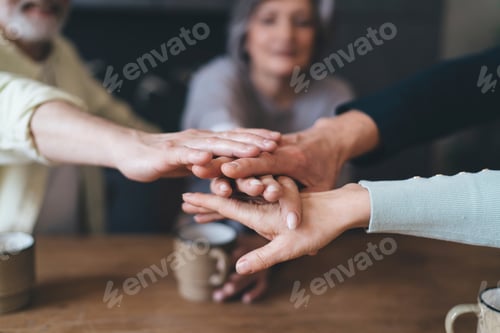 Preview: Crop unrecognizable aged friends stacking hands together while having hot drinks