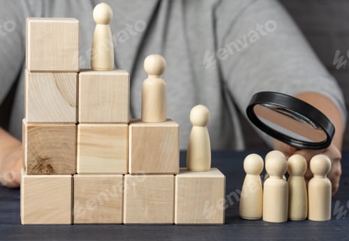Preview: Stairs made of wooden cubes and figurines of men, a hand with a magnifying glass examines the group