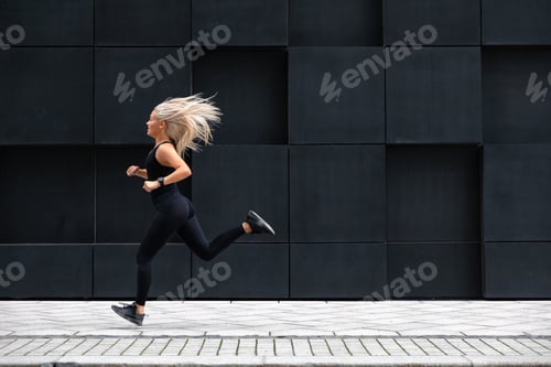 Preview: Focused woman running on the city street in modern environment