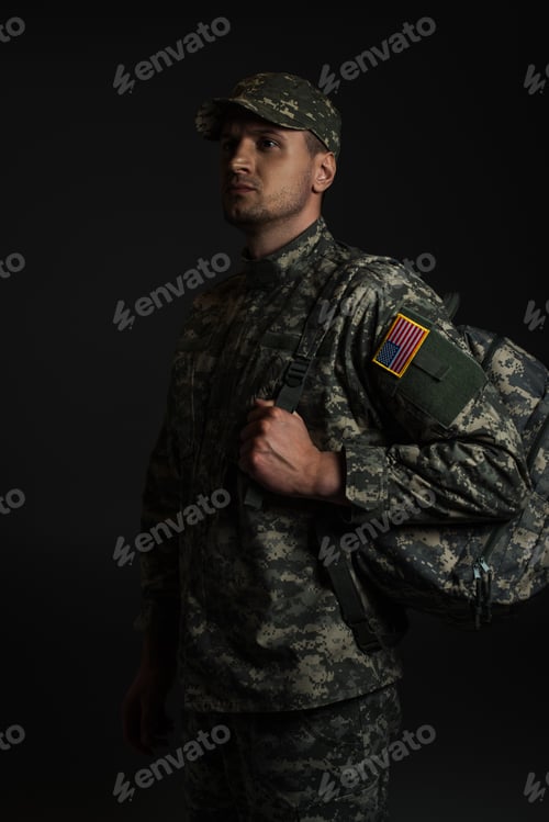 Preview: patriotic soldier in uniform with American flag holding backpack isolated on black