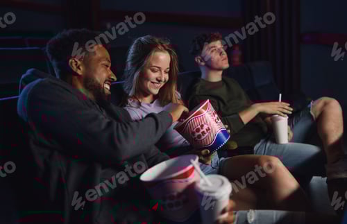 Preview: Cheerful young couple with popcorn in the cinema, talking