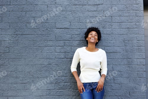 Preview: Cheerful young black woman standing against gray wall