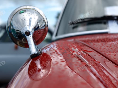 Preview: Closeup of a wing mirror on a red classic car with water droplets