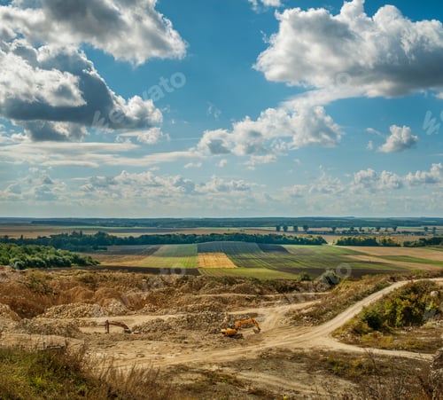 Preview: quarry and excavator working and fields under blue sky with clouds.