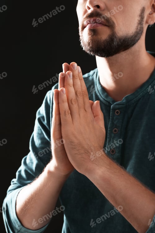 Preview: Man with hands clasped together for prayer on black background