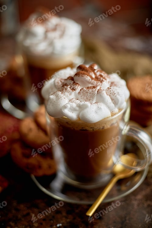 Preview: Two tall glasses with hot chocolate, whipped cream and cinnamon powder on top